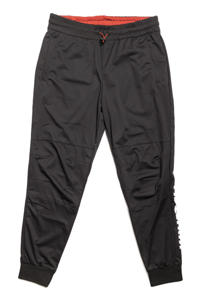 Die schwarze Fleecehose für Herren hat einen elastischen Bund, gerippte Beinabschlüsse, einen weißen Text auf dem linken Bein und ein kleines rotes Logo darüber, das die Essenz des Shops Kuhstall Kitzloch widerspiegelt. Diese Hose mit entspannter Passform wird auf einem schlichten weißen Hintergrund präsentiert.