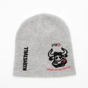Die graue Beanie mit dem Namen „Mütze ‚Kuhkopf‘ grau“ zeigt ein verspieltes Cartoon-Stiergesicht mit heraushängender Zunge und einem gepiercten Ohr vor weißem Hintergrund. „KUHSTALL“ verläuft vertikal, während „HOME OF WAHNSINN“ unten erscheint und den mutigen Geist des Kuhstalls Kitzloch verkörpert.
