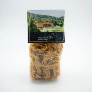 Auf der durchsichtigen Plastikverpackung der Alpencurry Bandnudeln ist als Etikett eine gemütliche Holzhütte abgebildet, umgeben von Bäumen und einem Feld. Das Wort „MASHOF“ ist in kräftigen Lettern auf einem schlichten, hellen Hintergrund gedruckt.